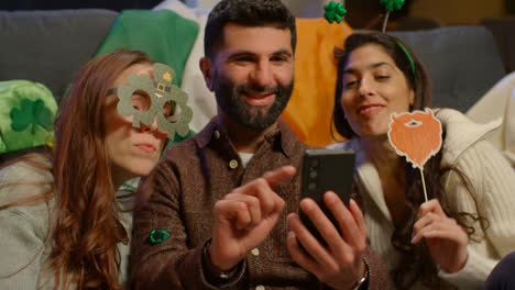 Group-Of-Friends-Dressing-Up-At-Home-Or-In-Bar-Celebrating-At-St-Patrick's-Day-Party-Posing-For-Selfie-On-Phone-2